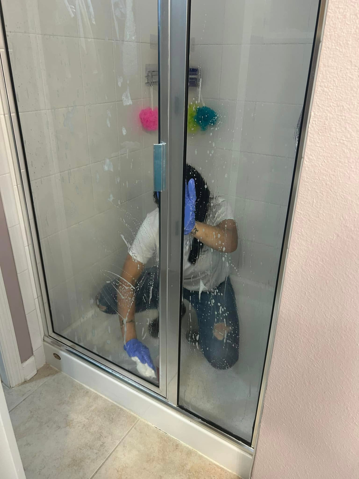 Cleaner scrubbing the inside of a glass shower enclosure